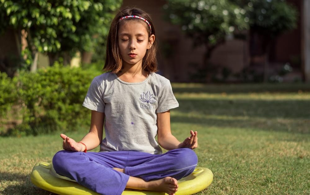 Girl meditating outside on yellow mat