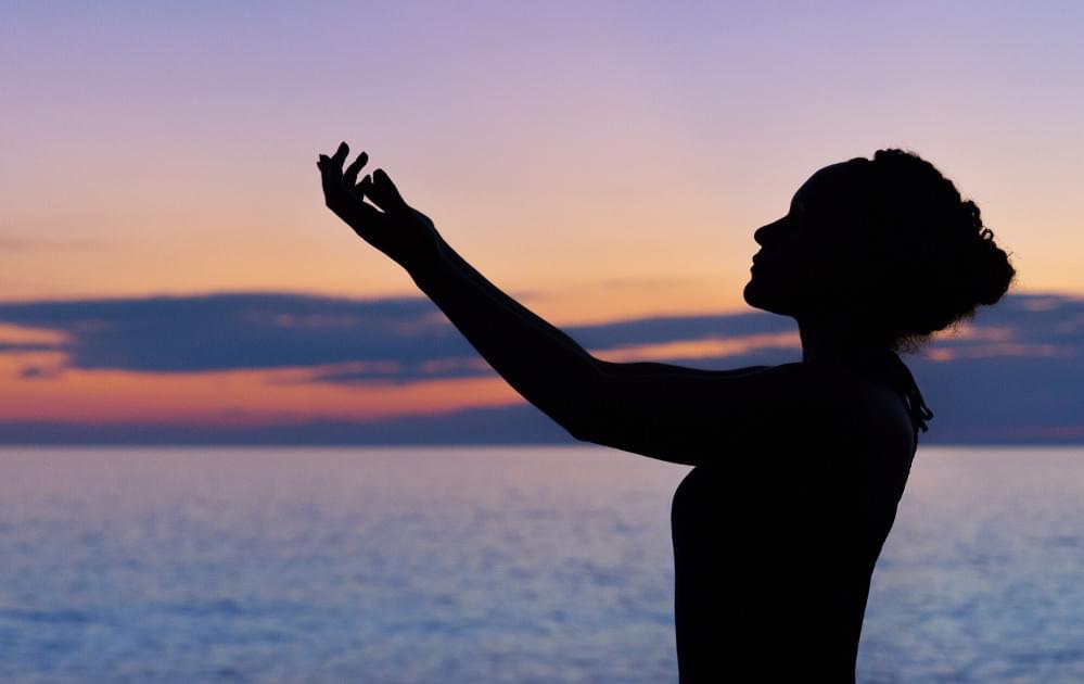 Silhouette of a woman raising right hand at a beach