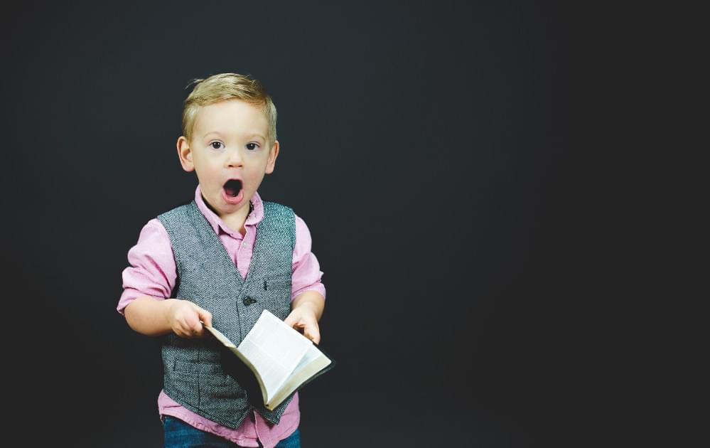 Surprised child holding a book on black background